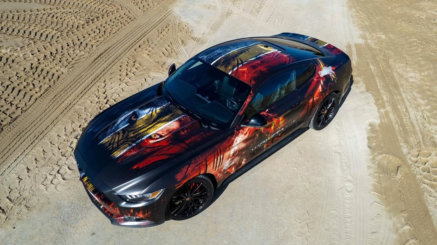 Ford Mustang Wolftang custom livery wrap — dronefoto driekwart voorkant met wolvenogen op de motorkap — FRD × WMR