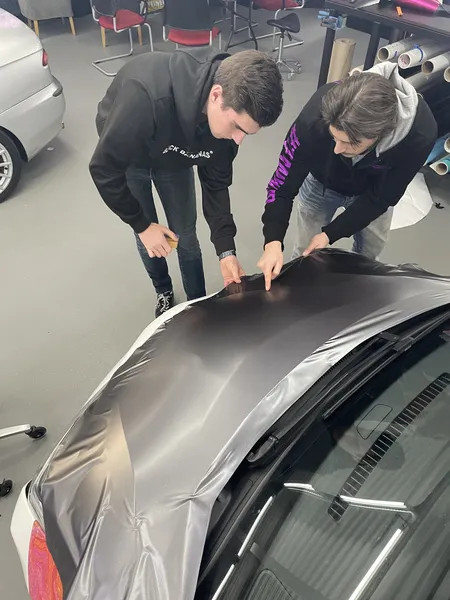 Twee studenten werken samen aan dakwrap — matte black vinyl